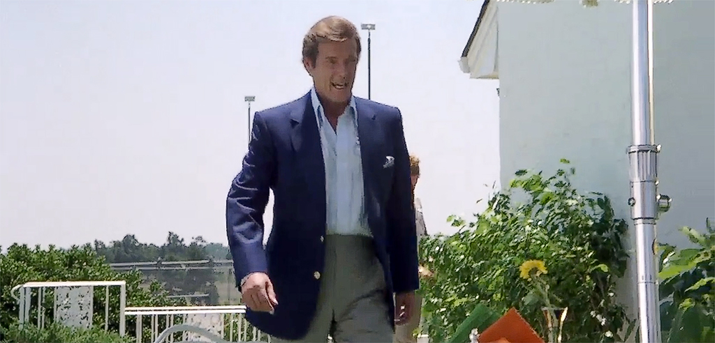 Roger Moore as a character impersonating James Bond in the movie Cannonball Run. He demonstrates casual with style. Navy Blue blazer with metal buttons, beige grey trousers and open collar shirt. And with pocket square.